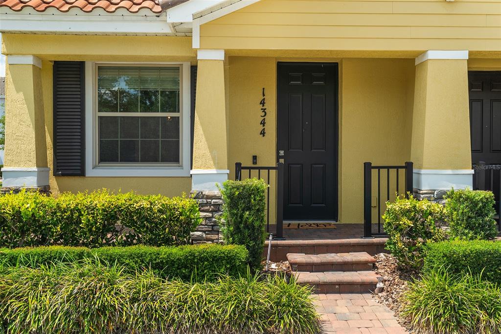 The exterior of a yellow house features a black front door and a brick walkway — 14344 SWANLEY STREET, ORLANDO, FL
