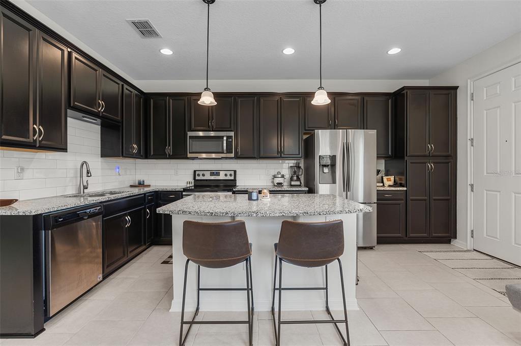 A kitchen with dark wood cabinets, granite countertops, a center island, and stainless steel appliances — 14344 SWANLEY STREET, ORLANDO, FL