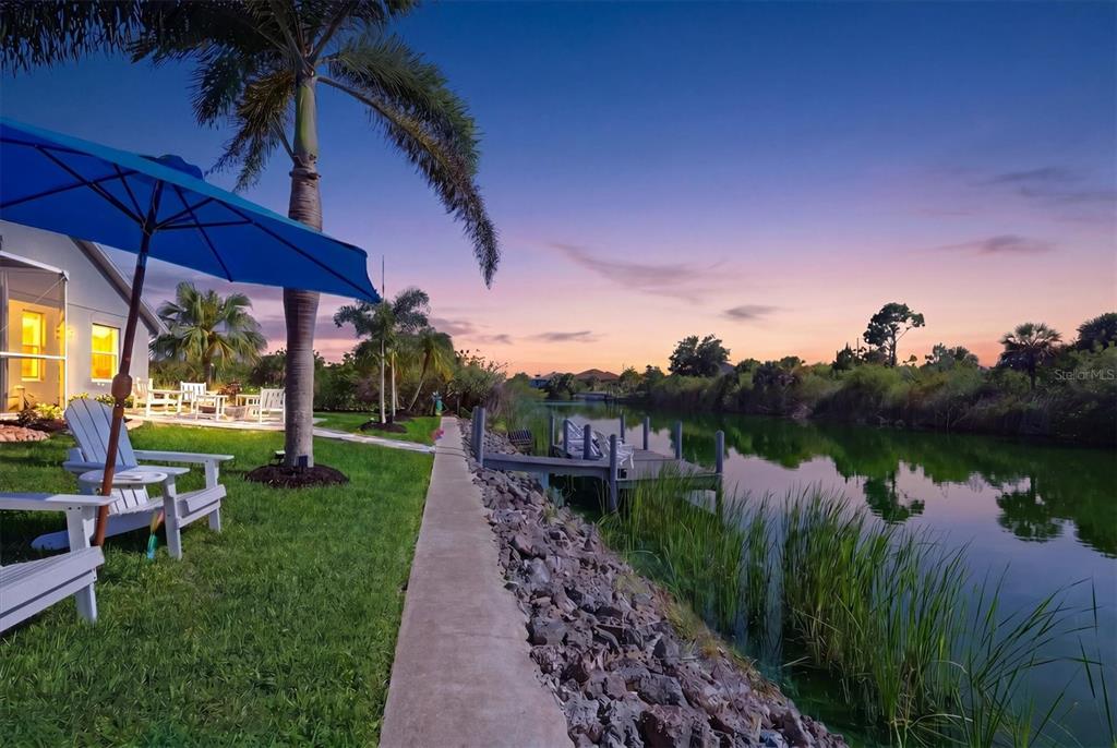 A backyard with a lawn, patio furniture, a palm tree, and a dock on a canal — 10083 KANSAS CITY STREET, PORT CHARLOTTE, FL