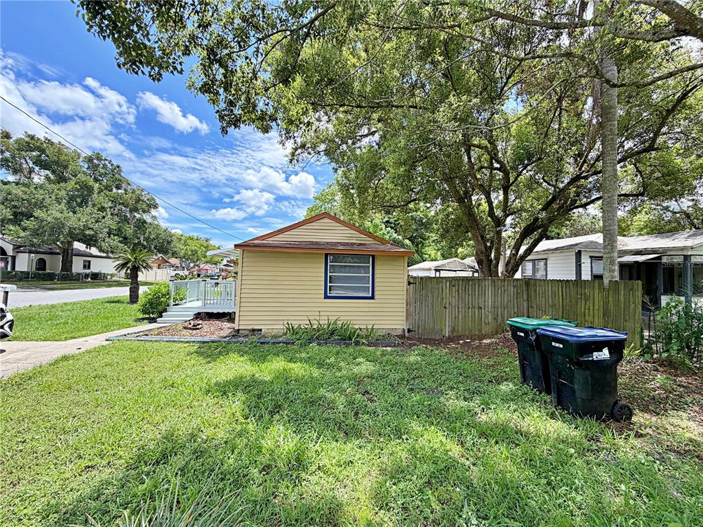A small, yellow-sided detached building sits in a grassy yard next to a wooden fence — 2400 SHANNON ROAD, ORLANDO, FL