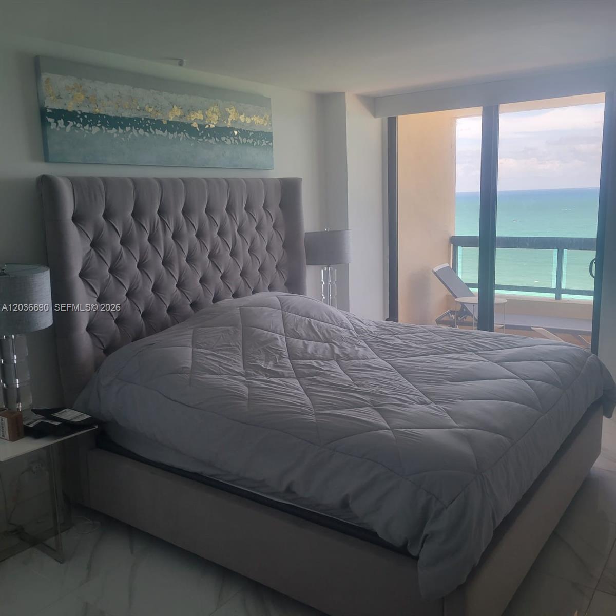 A bedroom features a tufted gray headboard, a quilted comforter, and a balcony overlooking the ocean — 2555 Collins Ave # 2207, Miami Beach FL 33140, MIAMI BEACH, FL