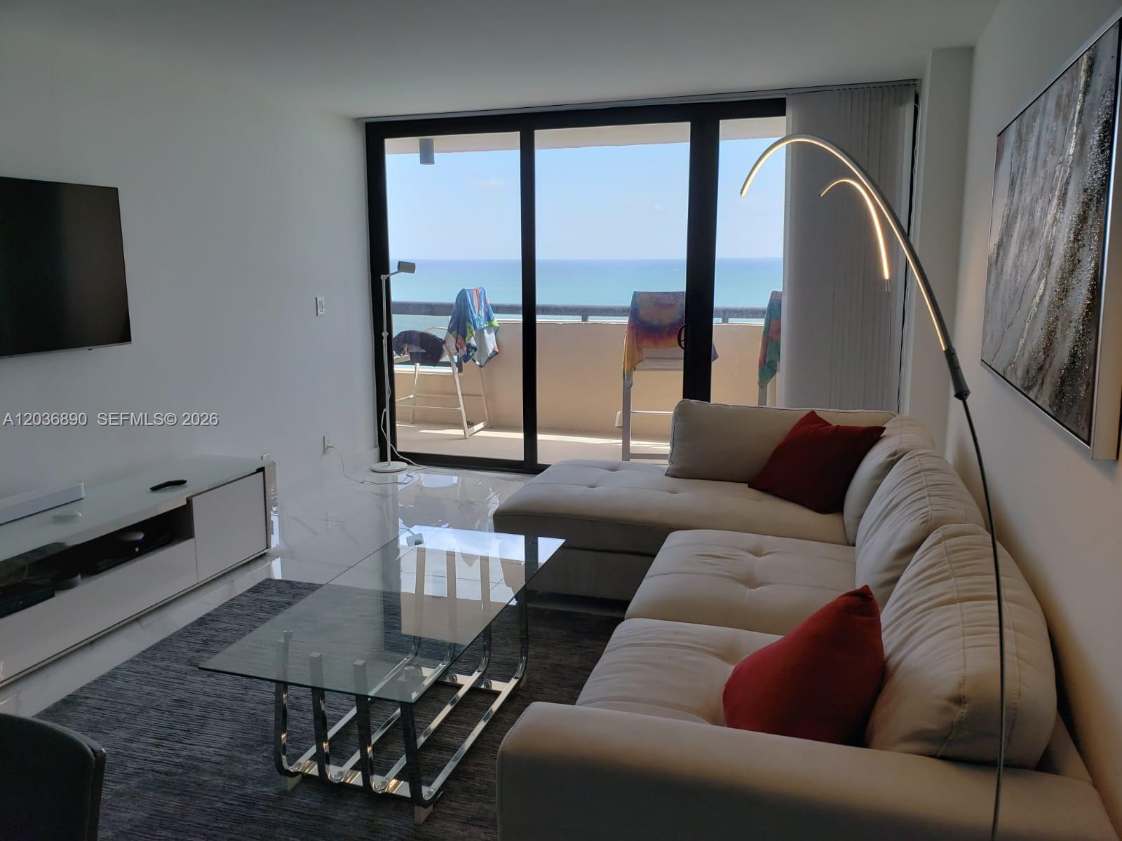 A living room features a white sectional sofa, glass coffee table, and balcony with ocean views — 2555 Collins Ave # 2207, Miami Beach FL 33140, MIAMI BEACH, FL