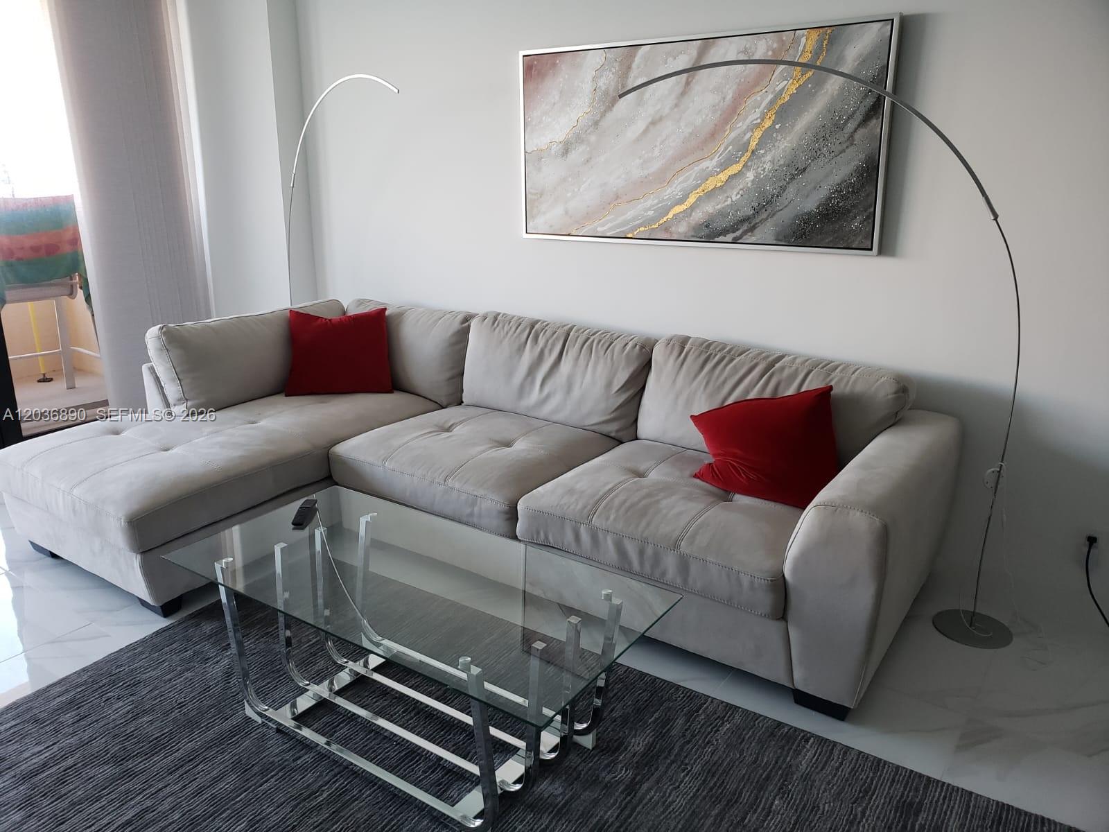 A living room features a light gray sectional sofa, a glass coffee table, and wall art — 2555 Collins Ave # 2207, Miami Beach FL 33140, MIAMI BEACH, FL