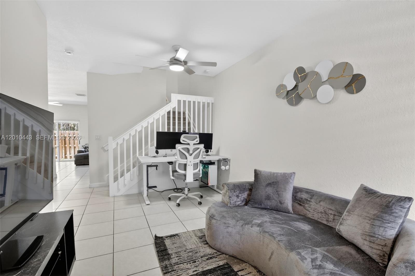 A living room features a curved gray sofa, a desk under a staircase, and tile flooring — 2691 NW 55th Way, Lauderhill FL 33313, LAUDERHILL, FL