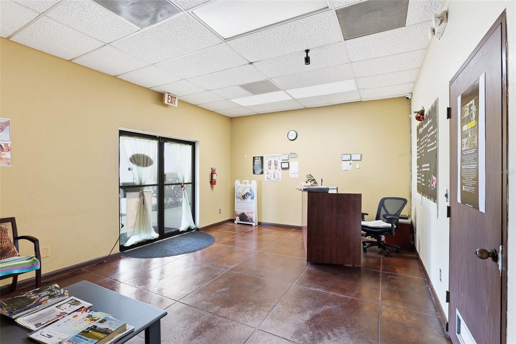 A reception area features a dark wood desk, tile flooring, and a glass-paned exit door — 0000 WICKHAM RD, MELBOURNE, FL