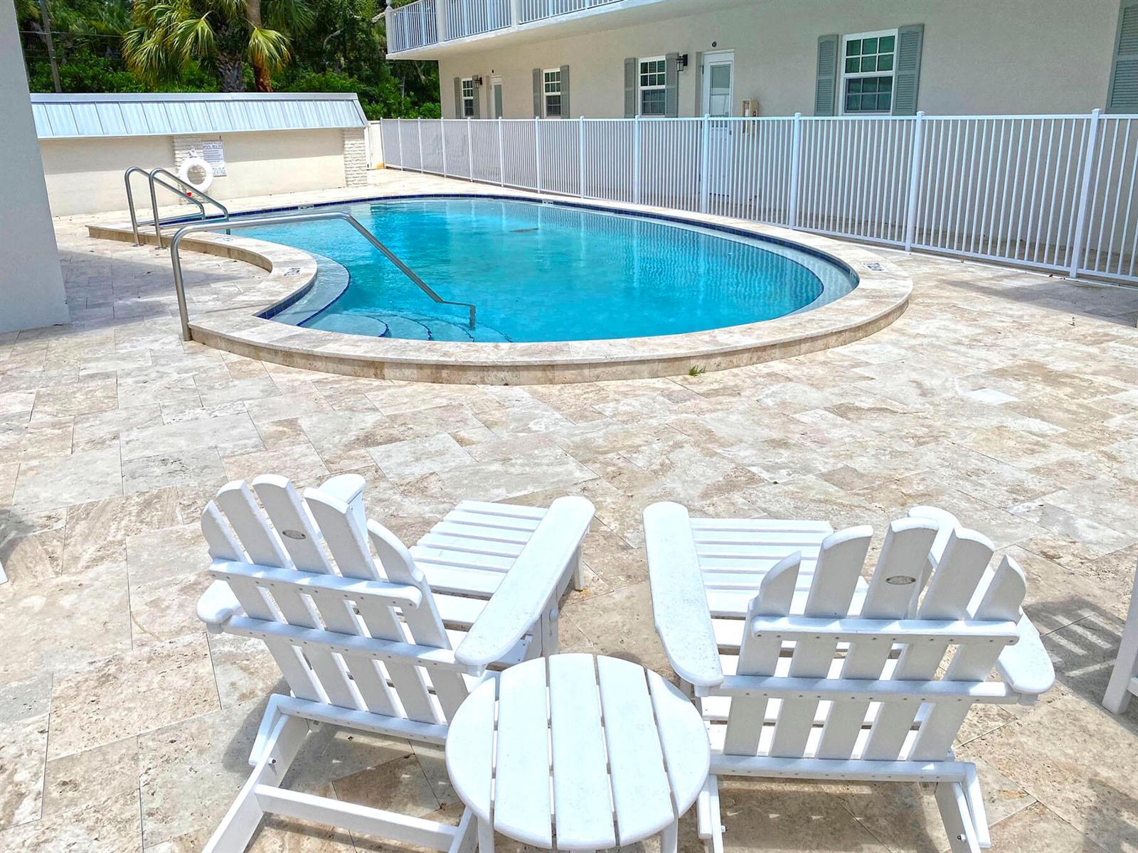 Two white Adirondack chairs face a kidney-shaped swimming pool on a stone patio — 900 Jasmine Lane # 9a, Vero Beach FL 32963, VERO BEACH, FL
