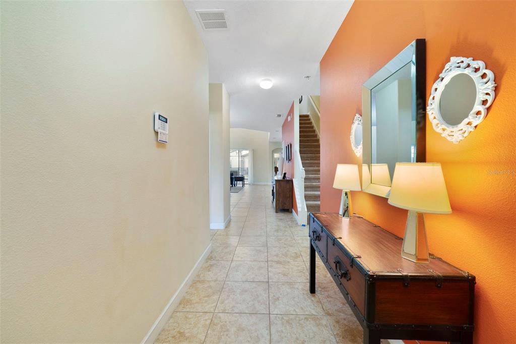 A hallway with tile flooring leads toward a staircase and an orange accent wall — 8928 BISMARCK PALM ROAD, KISSIMMEE, FL