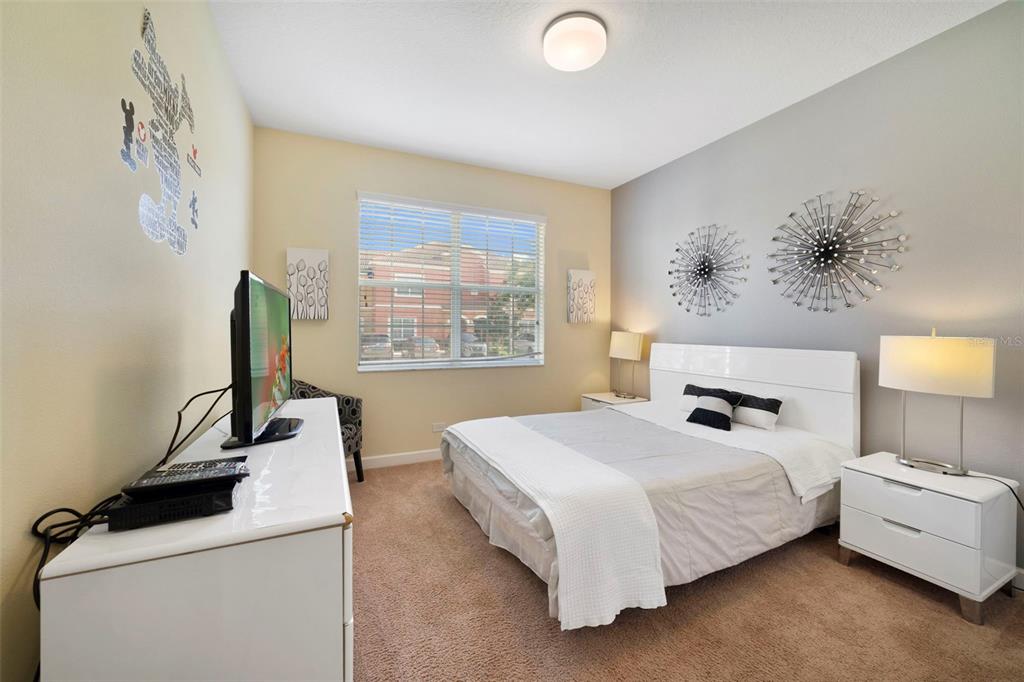 A bedroom features a white bed, matching nightstands, a dresser with a television, and carpet — 8928 BISMARCK PALM ROAD, KISSIMMEE, FL