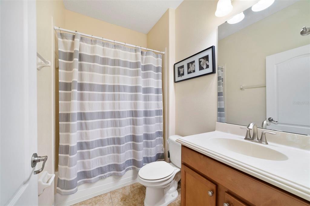 A bathroom features a wood vanity, a toilet, and a shower with a striped curtain — 8928 BISMARCK PALM ROAD, KISSIMMEE, FL