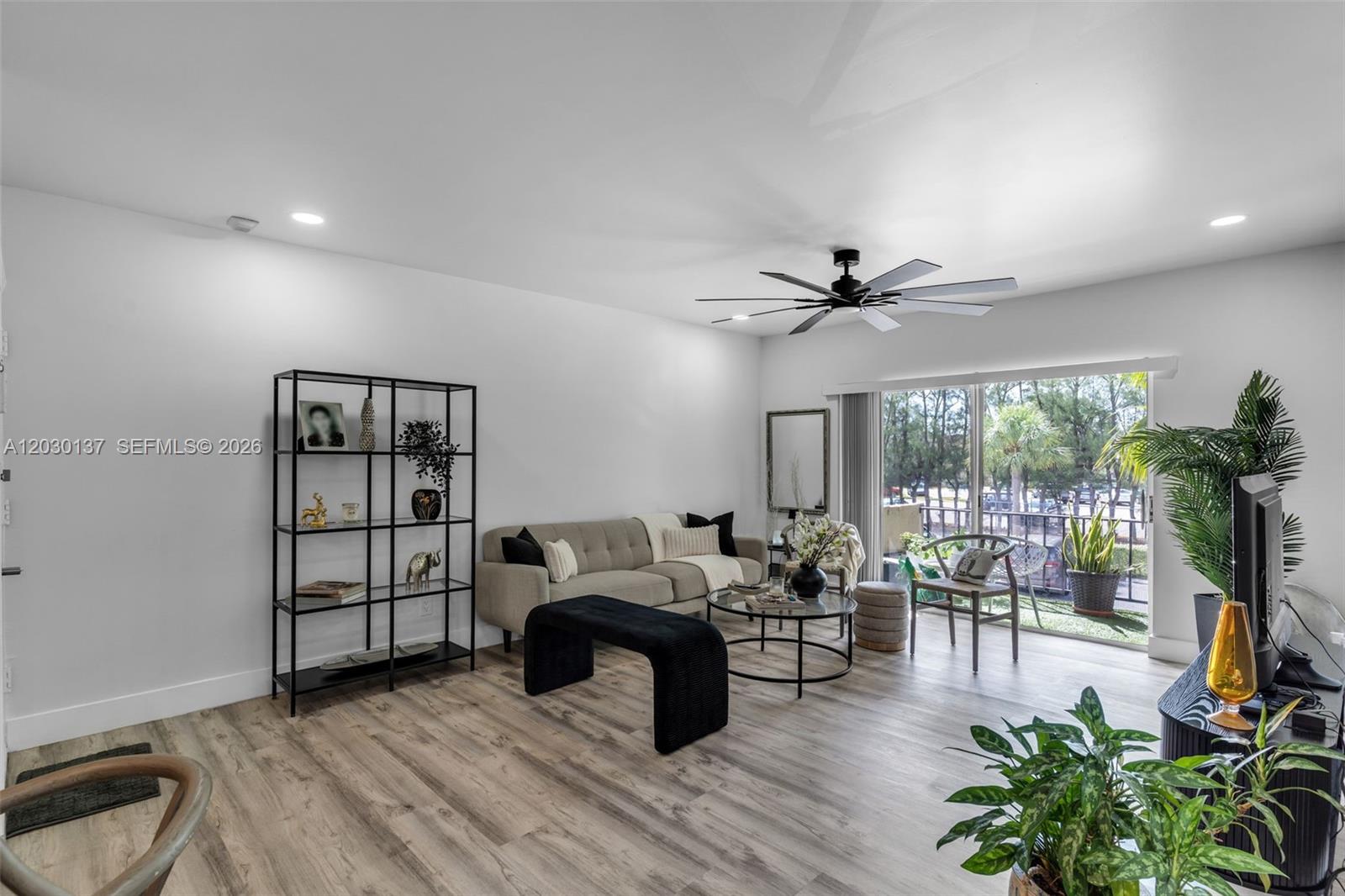 A living room features light wood-look flooring, a beige sofa, a black bookshelf, and sliding doors — 13726 SW 90th Ave # 28, Miami FL 33176, MIAMI, FL