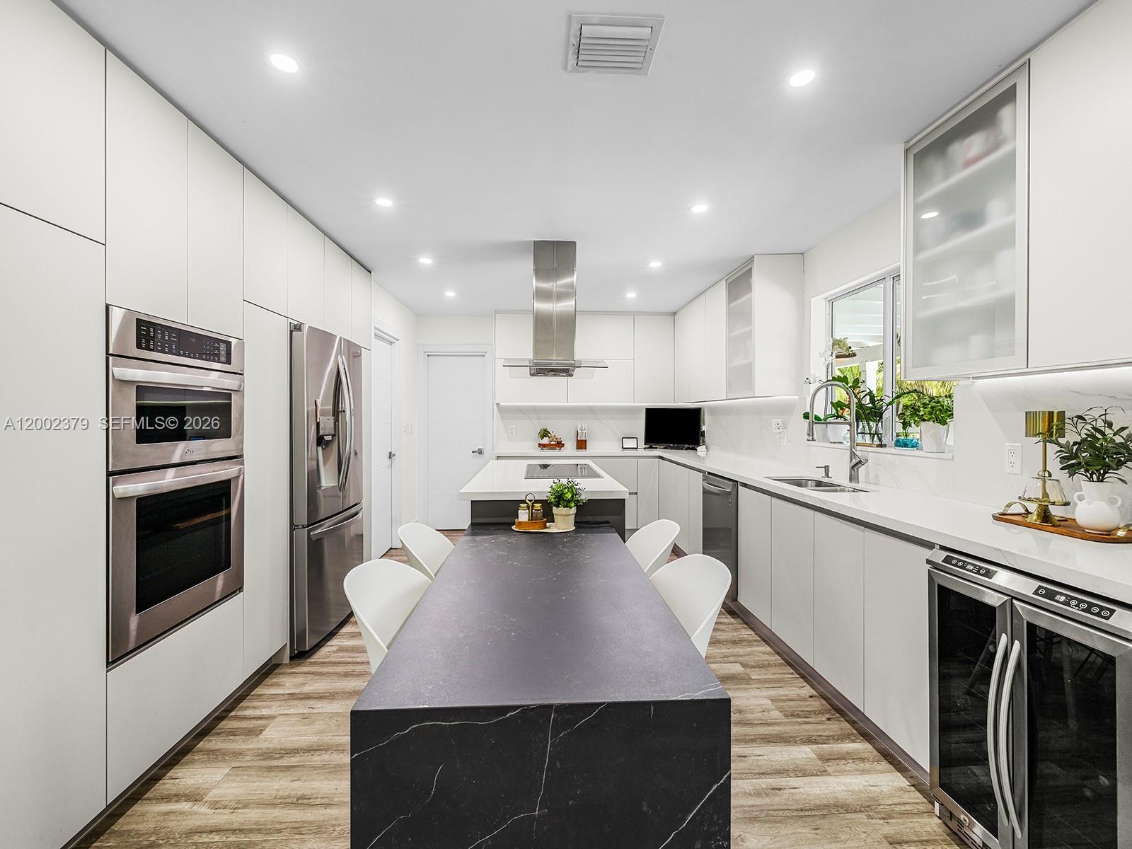 A modern kitchen features white cabinetry, a dark stone island, and stainless steel appliances — 7495 SW 73rd Ter, Miami FL 33143, MIAMI, FL