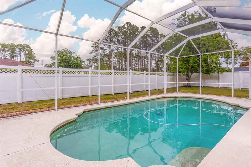 A swimming pool enclosed by a screen cage sits in a backyard with a white fence — 4 EAGLE PLACE, PALM COAST, FL