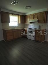 A kitchen features wood cabinets, a white stove, and dark wood-look flooring — 230 MONROE AVENUE, BROOKSVILLE, FL