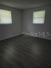 An empty bedroom features gray wood-look flooring, light-colored walls, and two windows with blinds — 230 MONROE AVENUE, BROOKSVILLE, FL