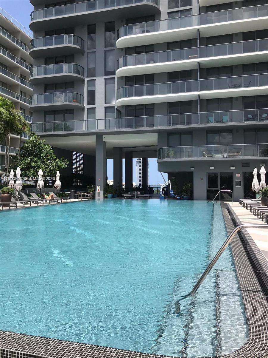 A swimming pool sits in front of a modern multi-story apartment building with balconies — 121 NE 34 St # 2215, Miami FL 33137, MIAMI, FL