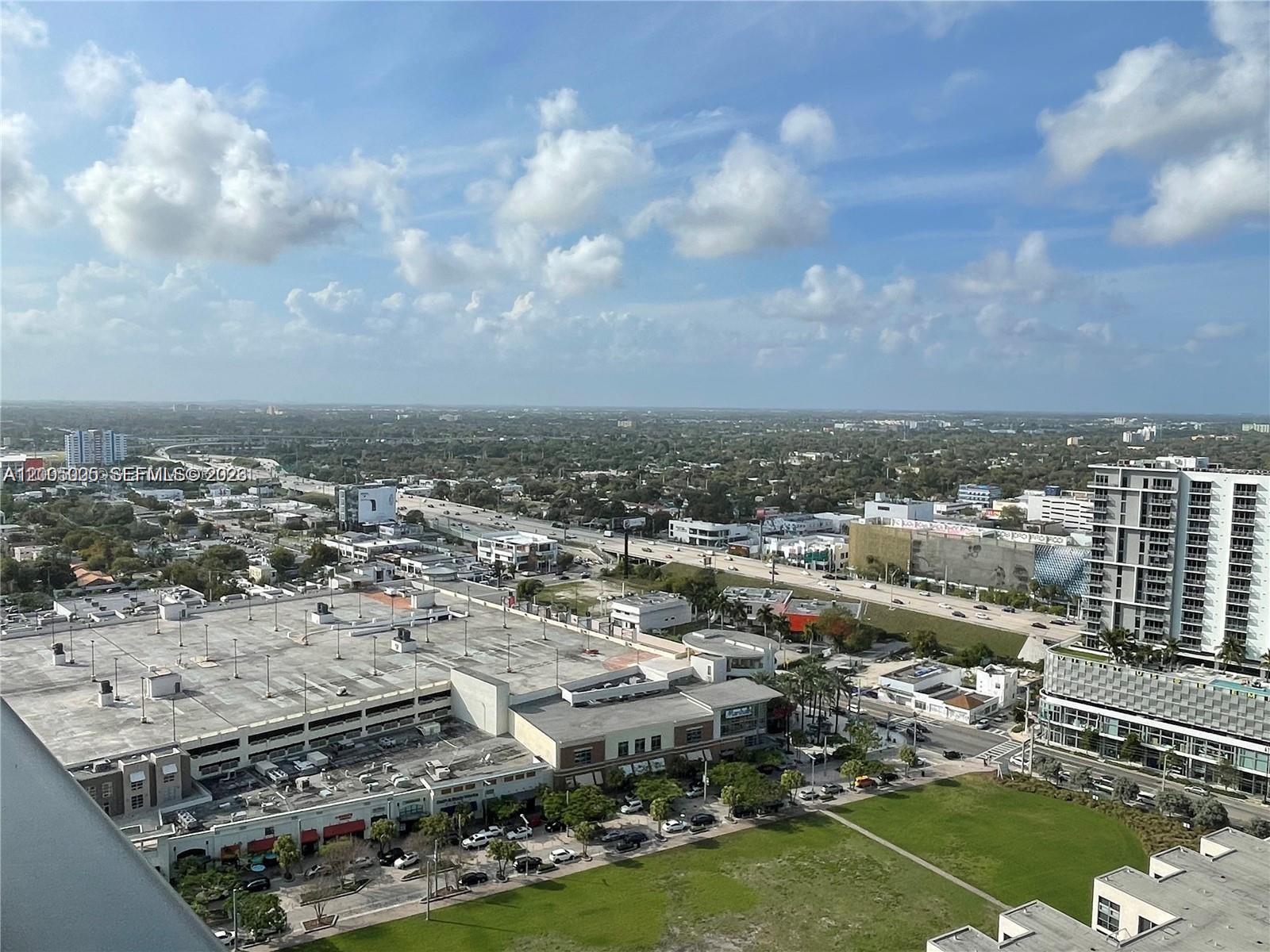 An elevated view shows a shopping center with a large parking garage and nearby highway — 121 NE 34 St # 2215, Miami FL 33137, MIAMI, FL