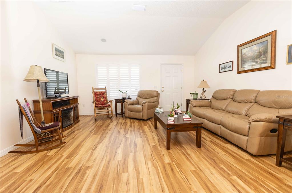 A living room features light wood-look flooring, a tan leather sofa, and two wooden rocking chairs — 2706 MORVEN PARK WAY, THE VILLAGES, FL
