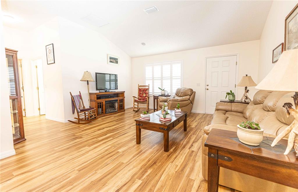 A living room features wood-look flooring, a tan leather sofa, a coffee table, and rocking chairs — 2706 MORVEN PARK WAY, THE VILLAGES, FL