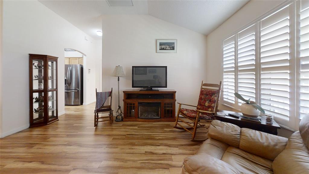 A living room features wood-look flooring, a television console, two rocking chairs, and plantation shutters — 2706 MORVEN PARK WAY, THE VILLAGES, FL