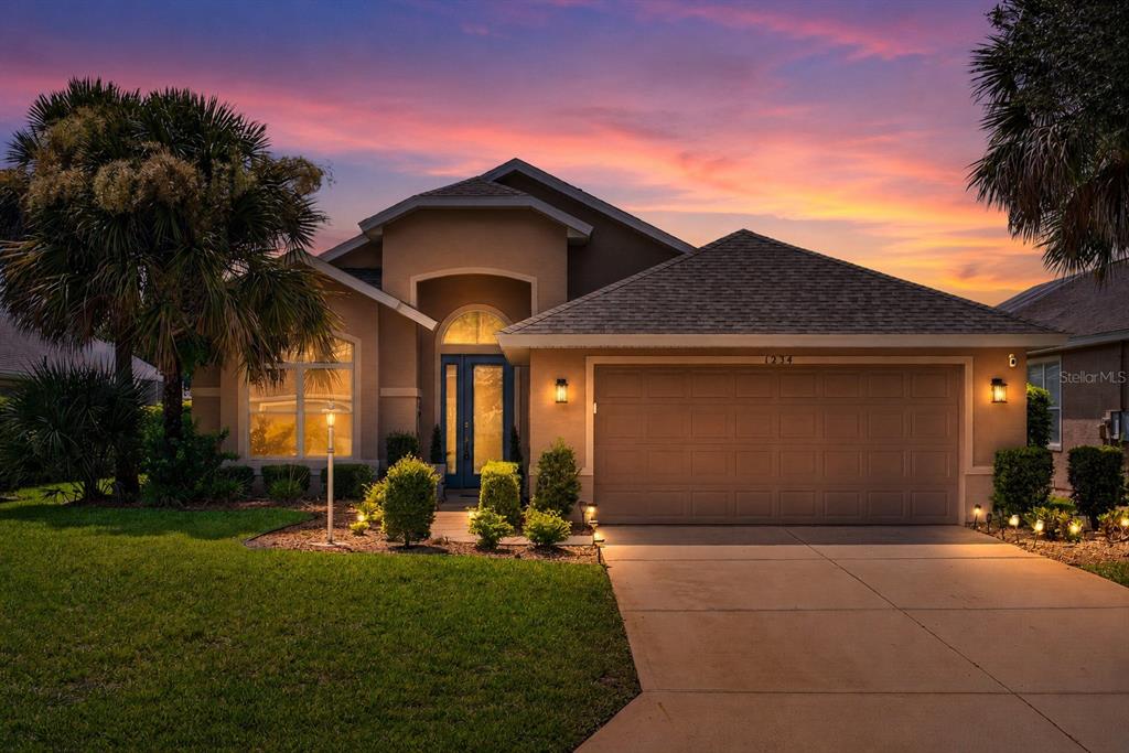 A single-story house with a tan stucco exterior, a two-car garage, and a sunset sky — 1234 CROWN POINTE LANE, ORMOND BEACH, FL