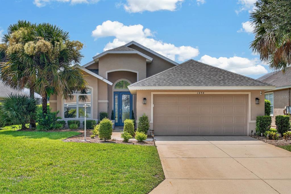 A single-story house with a beige stucco exterior, a two-car garage, and a blue front door — 1234 CROWN POINTE LANE, ORMOND BEACH, FL