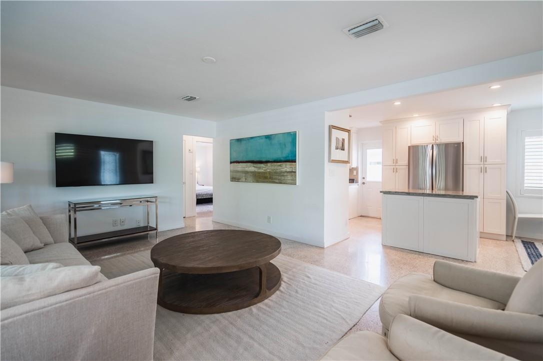 A living room with a television, circular wooden coffee table, and an open-concept white kitchen — 240 NE 25th Avenue, Pompano Beach FL 33062, POMPANO BEACH, FL