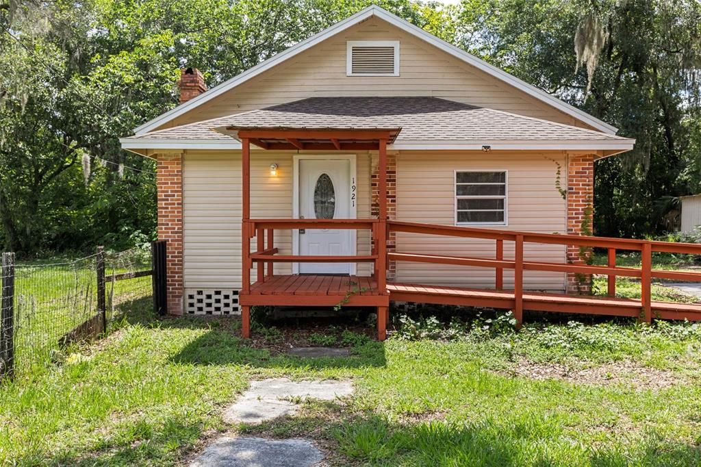 A single-story house with beige siding, a brick chimney, and a wooden wheelchair ramp — 1921 NE 8TH ROAD, OCALA, FL