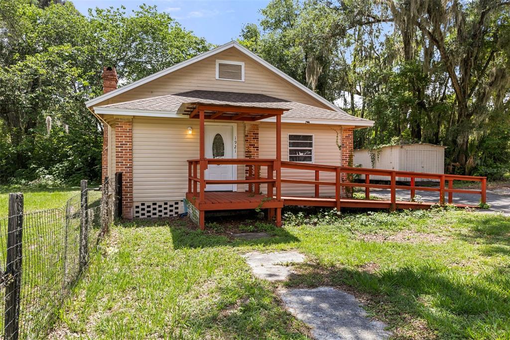 A small, tan-sided house with a brick chimney and a wooden wheelchair ramp leading inside — 1921 NE 8TH ROAD, OCALA, FL