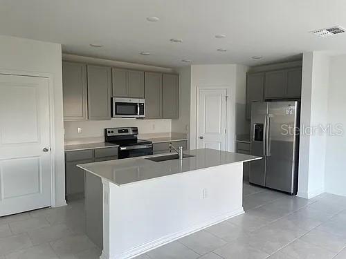 A modern kitchen features gray cabinets, stainless steel appliances, and a central quartz island — 642 BELL PRAIRIE CIRCLE, LAKE WALES, FL