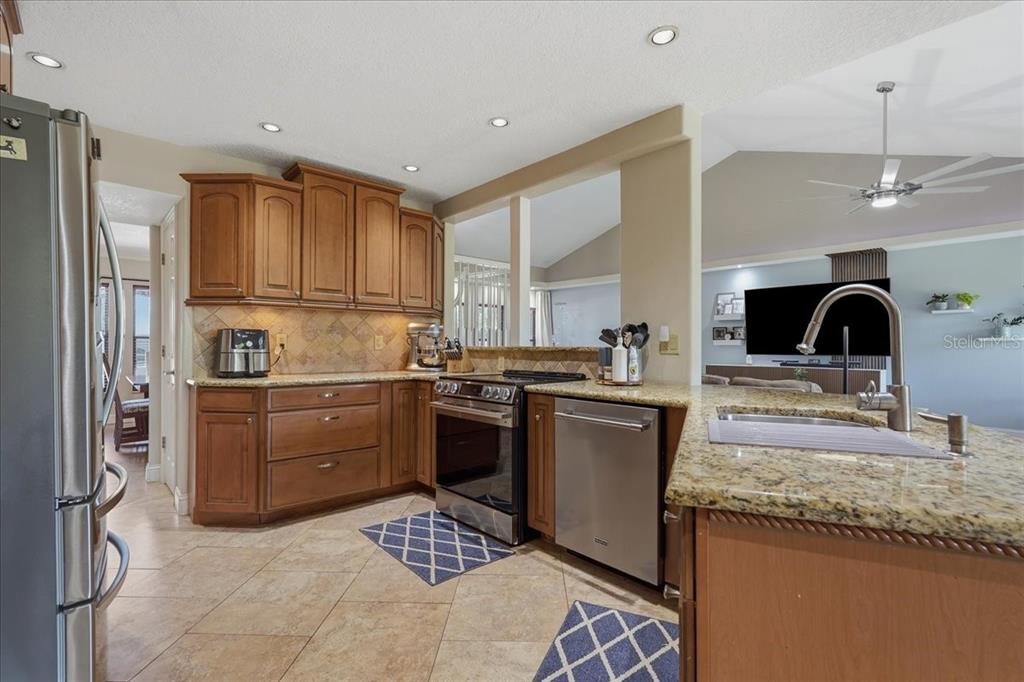 A kitchen features wood cabinets, granite countertops, stainless steel appliances, and tile flooring — 16043 PENWOOD DRIVE, TAMPA, FL