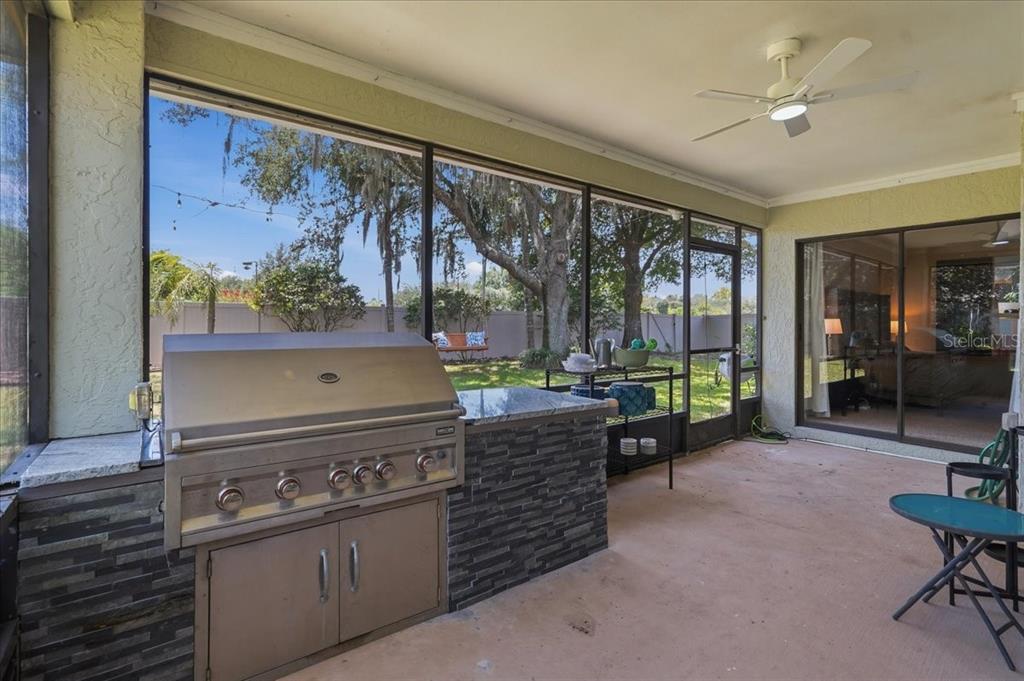 A screened-in patio features a built-in stainless steel grill, stone veneer base, and ceiling fan — 16043 PENWOOD DRIVE, TAMPA, FL
