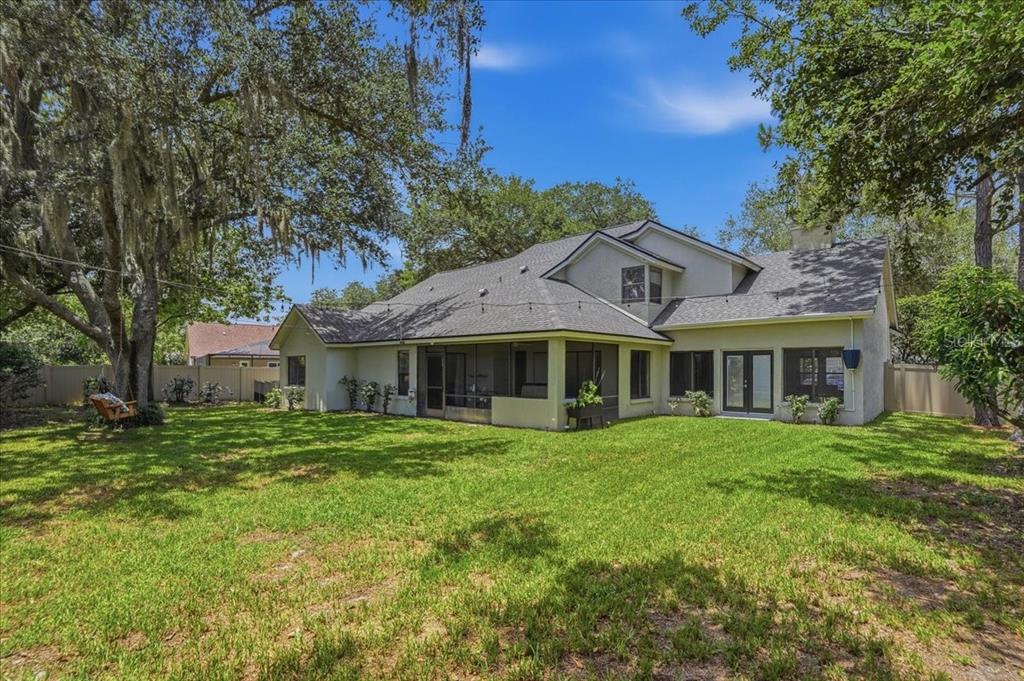 The backyard of a two-story house features a screened-in porch and large oak trees — 16043 PENWOOD DRIVE, TAMPA, FL
