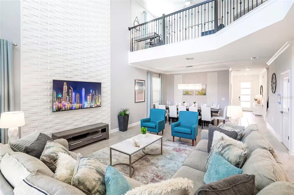 A living room with a white brick fireplace, blue armchairs, and a view of a loft — 4261 PROLOGUE WAY, KISSIMMEE, FL