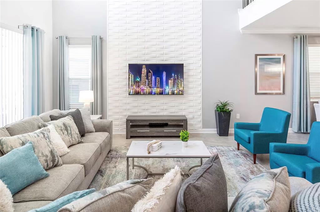 A living room features a white brick accent wall, a television, and blue armchairs — 4261 PROLOGUE WAY, KISSIMMEE, FL