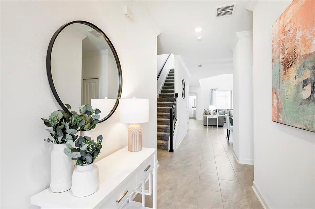 A white entryway features a console table, round mirror, and a staircase leading to living areas — 4261 PROLOGUE WAY, KISSIMMEE, FL