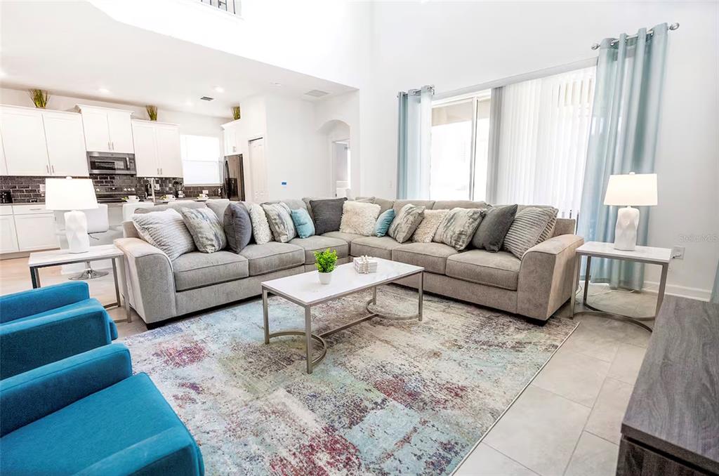 A bright living room features a large gray sectional, blue armchairs, and a marble coffee table — 4261 PROLOGUE WAY, KISSIMMEE, FL