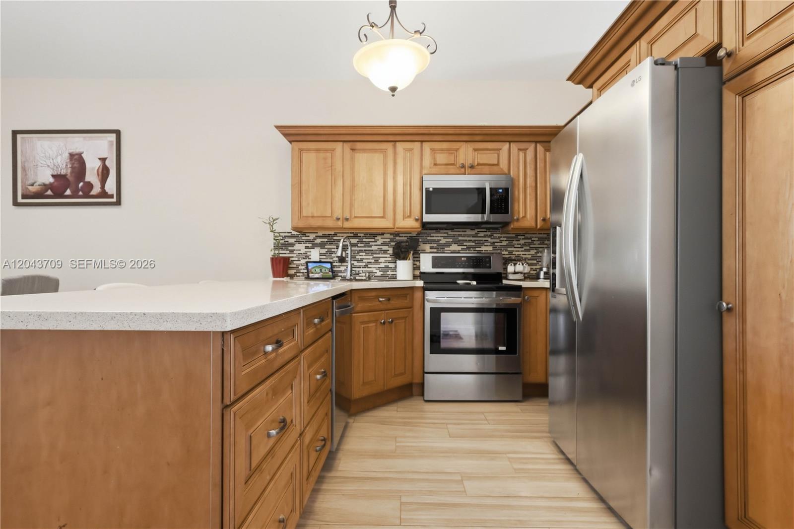 A kitchen features wood cabinets, stainless steel appliances, a white countertop, and tiled flooring — 610 SE 12th Ter, Homestead FL 33033, HOMESTEAD, FL