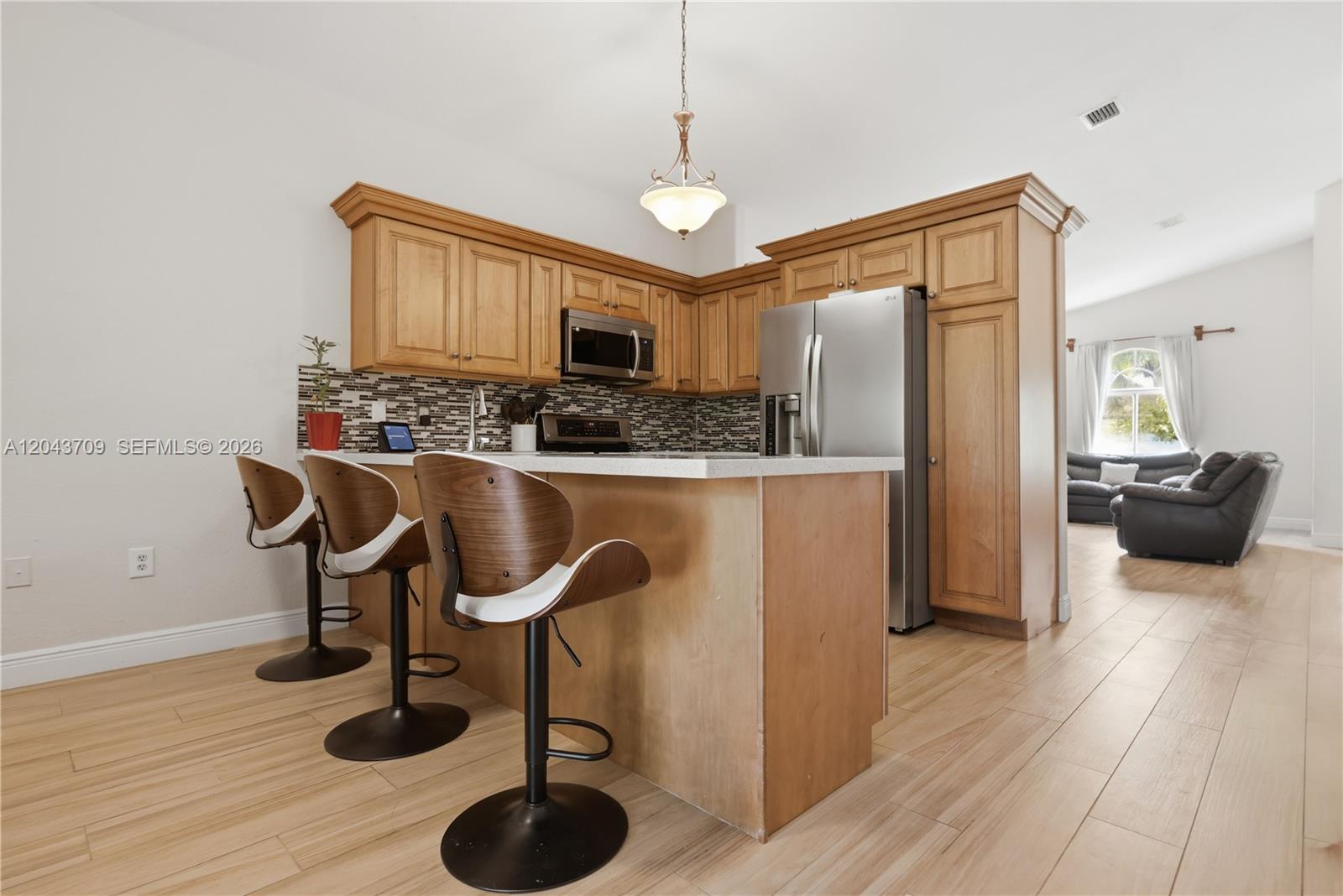 A kitchen features light wood cabinets, stainless steel appliances, and a breakfast bar with stools — 610 SE 12th Ter, Homestead FL 33033, HOMESTEAD, FL