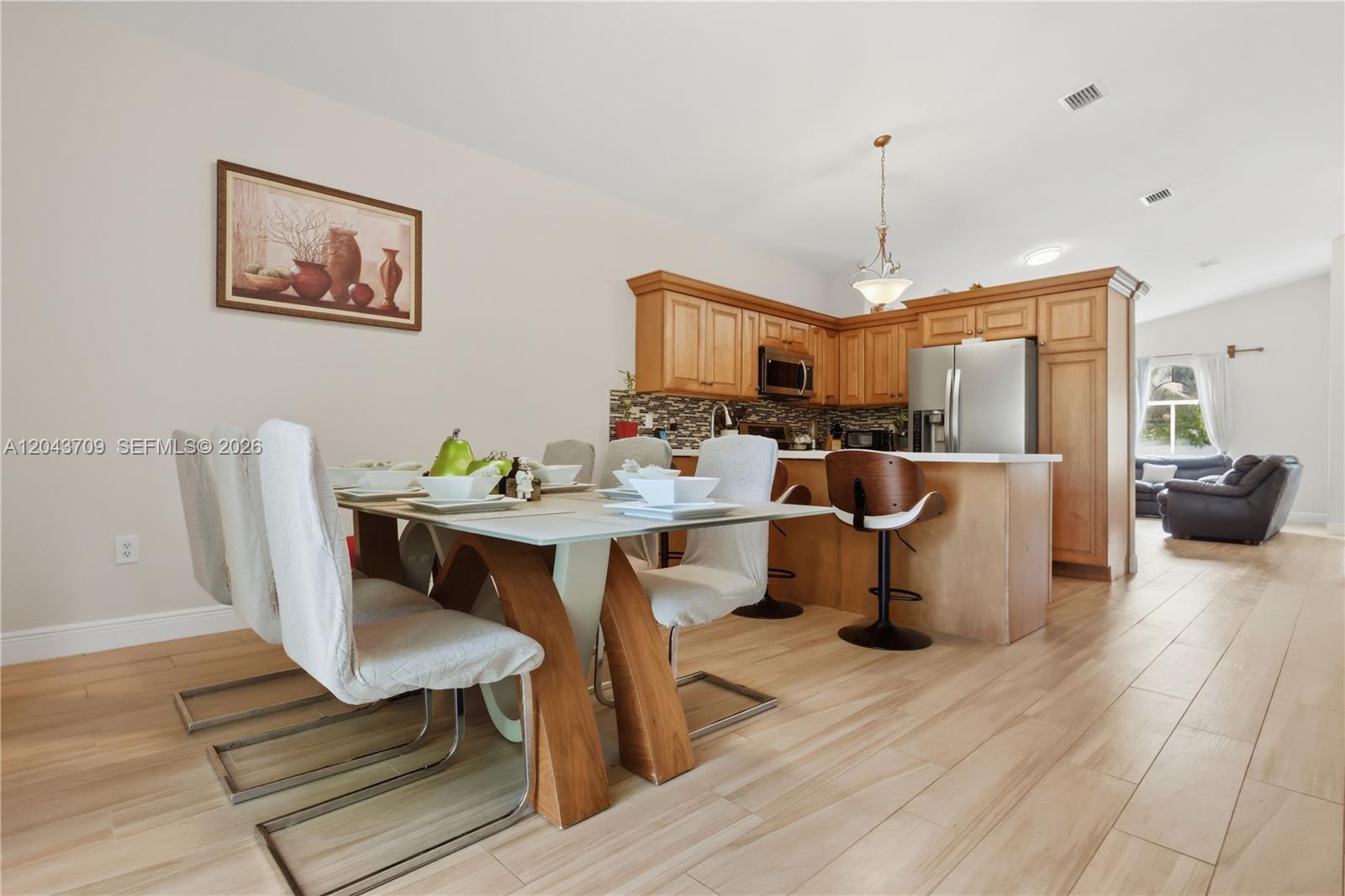 A dining area with a glass-top table sits adjacent to an open kitchen with wood cabinetry — 610 SE 12th Ter, Homestead FL 33033, HOMESTEAD, FL