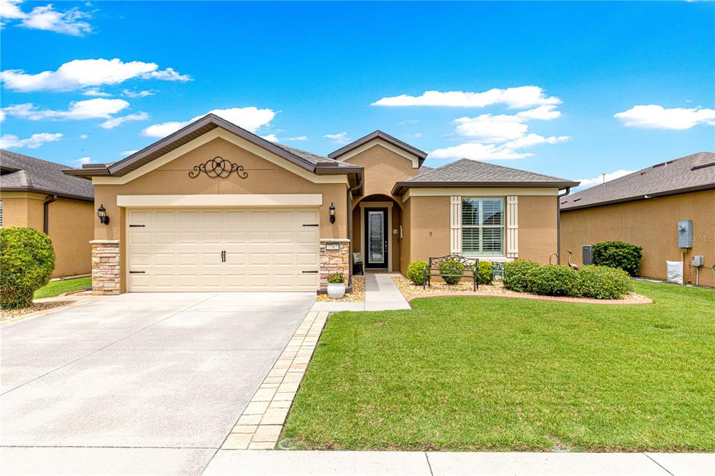 A single-story suburban house with a tan stucco exterior, a two-car garage, and a lawn — 7762 SW 97TH CIRCLE, OCALA, FL