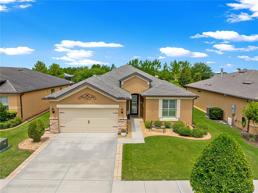 A single-story tan house with a two-car garage, stone accents, and a landscaped front yard — 7762 SW 97TH CIRCLE, OCALA, FL