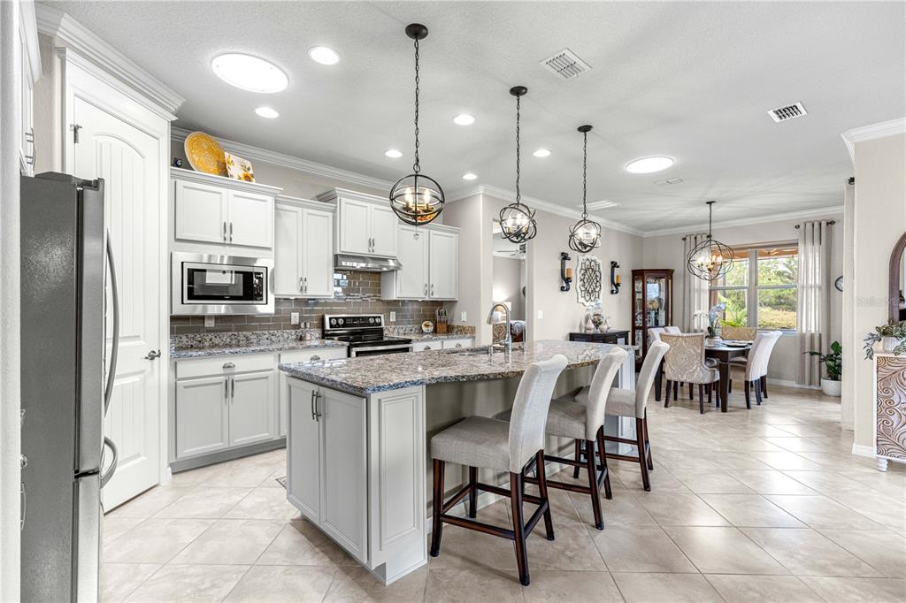 A kitchen features white cabinetry, granite countertops, a central island with bar seating, and pendant lighting — 7762 SW 97TH CIRCLE, OCALA, FL