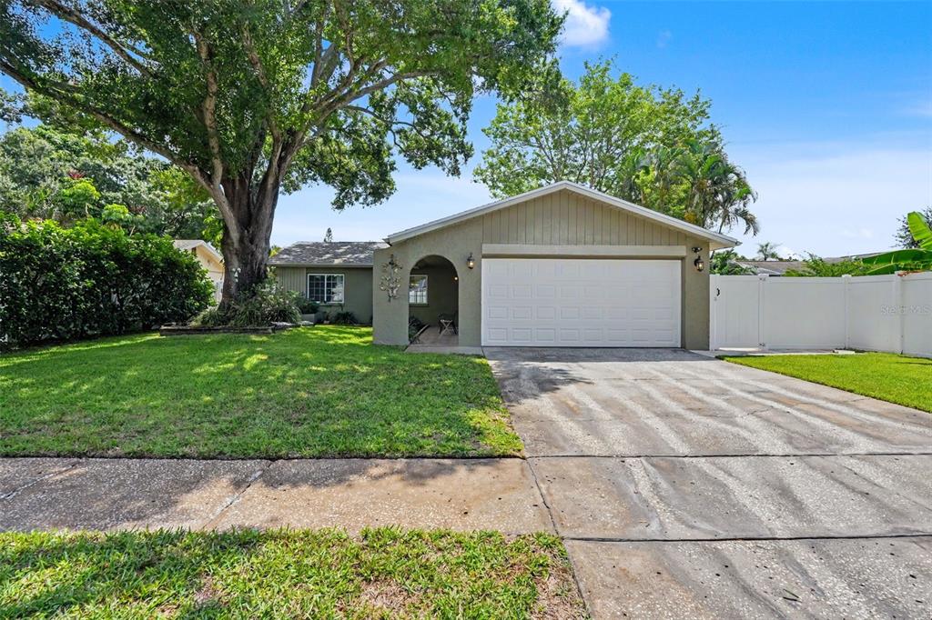 A single-story house with a white garage door, a front porch, and a large tree — 12431 DEL VERDE DRIVE, LARGO, FL