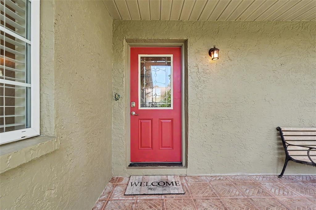 A red front door with a glass insert sits on a covered porch with tile — 12431 DEL VERDE DRIVE, LARGO, FL