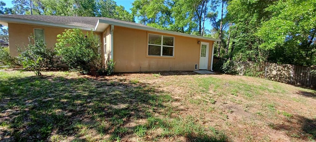 The exterior of a tan, single-story house features a white door and a large window — 6521 E GRAYSON STREET, INVERNESS, FL