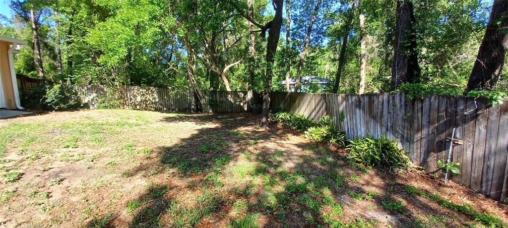 A backyard features a wooden fence, sparse grass, and mature trees under a clear sky — 6521 E GRAYSON STREET, INVERNESS, FL
