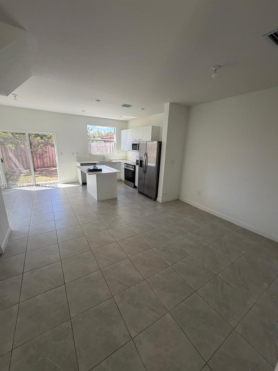 An open-concept kitchen with white cabinets, stainless steel appliances, and tile flooring — 12148 NW 24TH PL # 12148, Miami FL 33167, MIAMI, FL