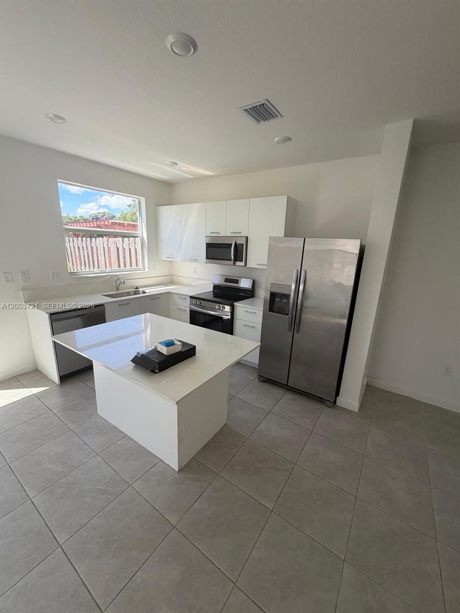 A modern kitchen features white cabinets, stainless steel appliances, and a central quartz island — 12148 NW 24TH PL # 12148, Miami FL 33167, MIAMI, FL