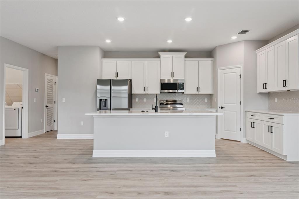 A modern kitchen features white cabinets, stainless steel appliances, a center island, and light flooring — 489 MARION OAKS TRAIL, OCALA, FL