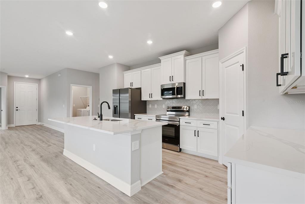 A modern kitchen features white cabinets, stainless steel appliances, a quartz island, and light flooring — 489 MARION OAKS TRAIL, OCALA, FL